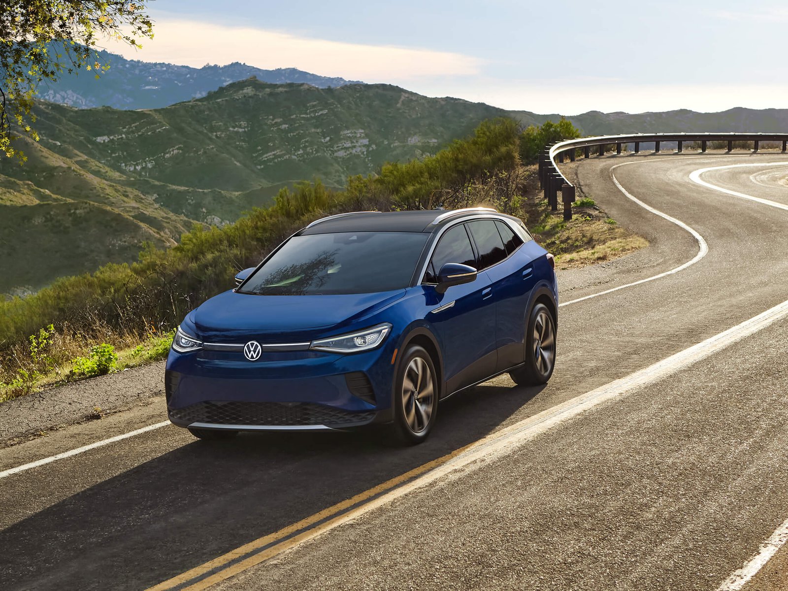 An ID.4 in Dusk Blue Metallic drives along a single-lane highway with mountains in the background.