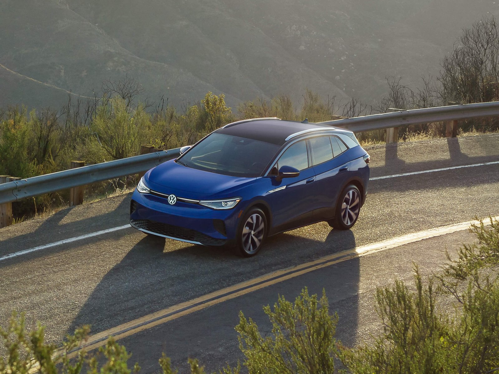 An ID.4 in Dusk Blue Metallic drives along a single-lane highway.