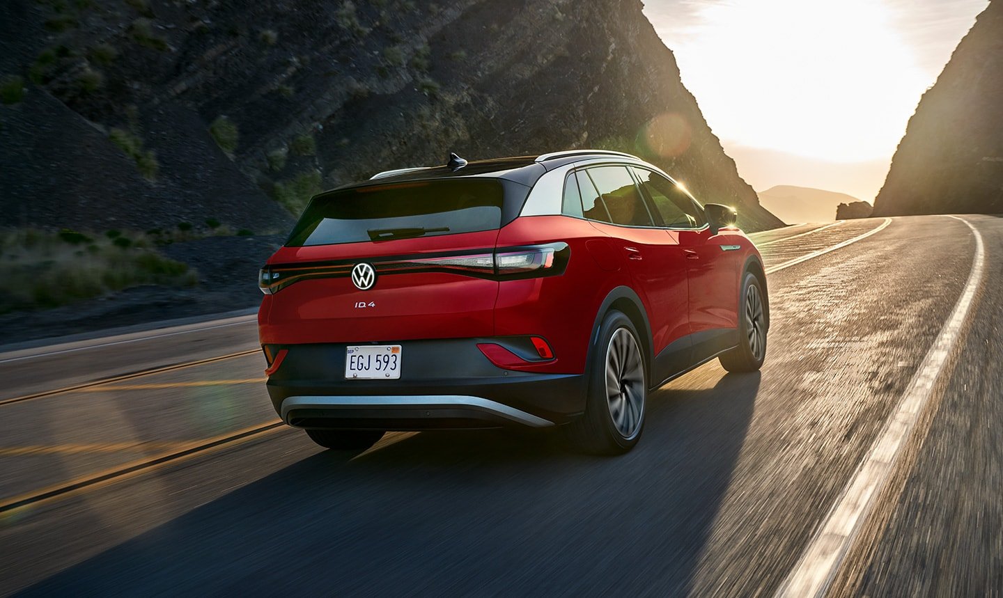 A rear view shot of an ID.4 Pro S Plus in Aurora Red Metallic driving up a two- lane mountain road with the sun shining in the distance.