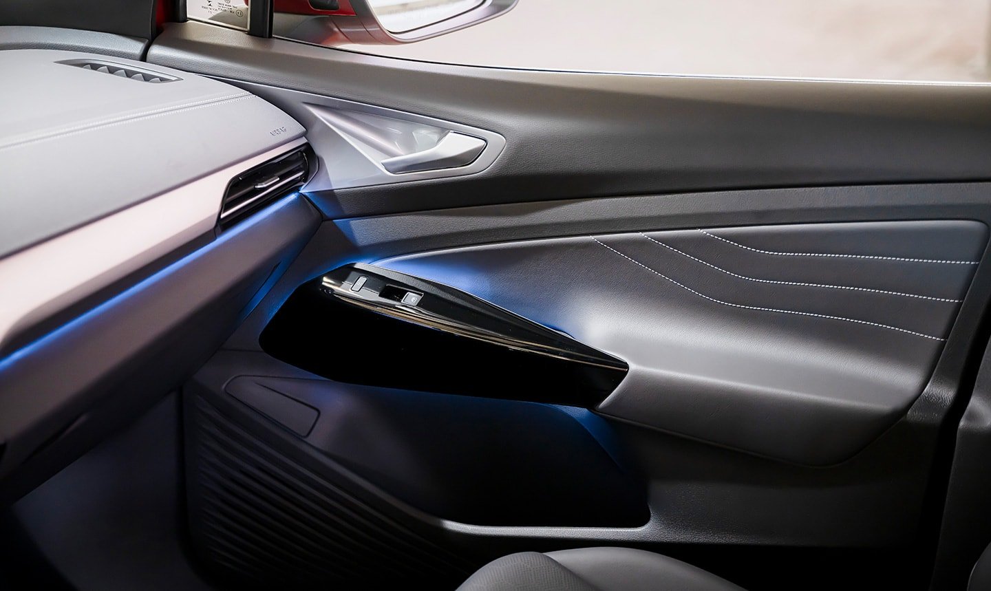 An interior shot of an ID.4 showing blue glow of ambient lighting along dash and door, with focus on the passenger-side door.